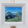 The Lost Valley in a pale frame on an easel: green mountains under a blue sky.