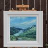 Loch Leven in a pale frame on an easel: a green glen with water winding between the hills.