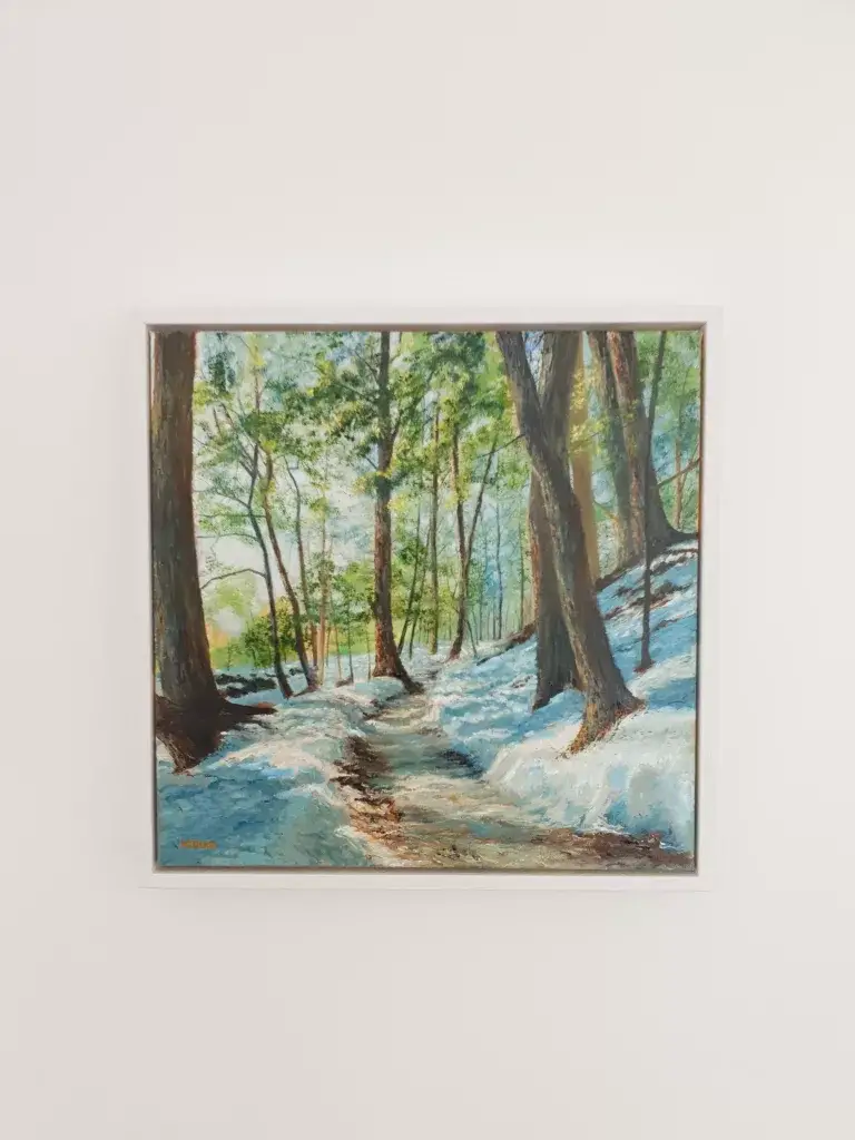 A woodland path through thawing snow, a stream running between bare trees.
