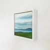 Coast in its white float frame, seen from the side on a white wall.