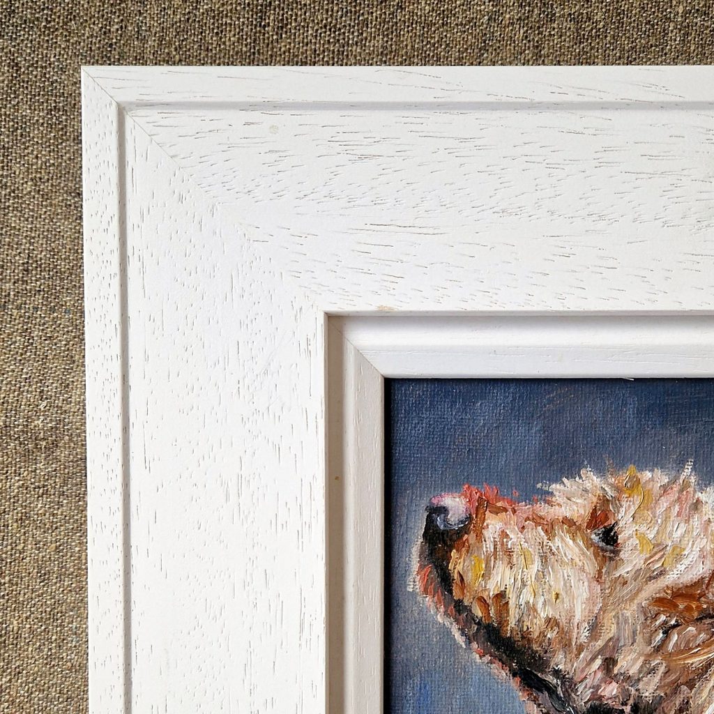 Corner of a white classic frame with a white inner slip around an oil portrait of a terrier